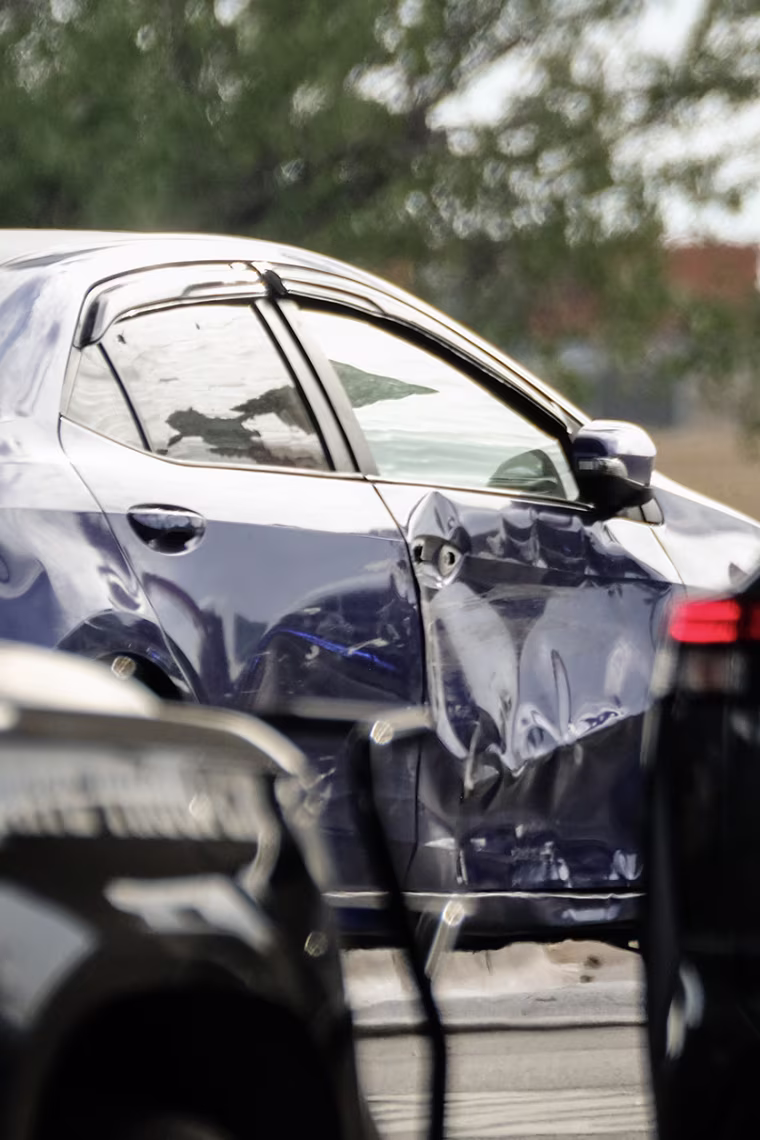 Bullet holes and scratches on the exterior of a blue sedan.