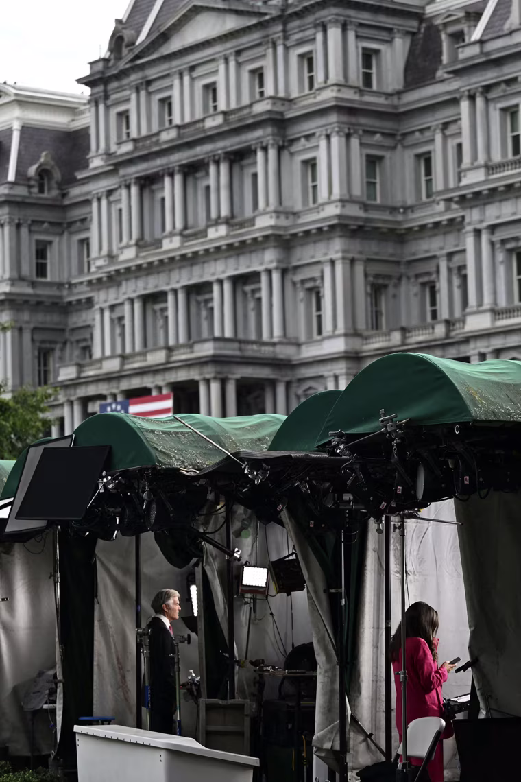 TV broadcast reporters stand inside green-roofed tents on the White House lawn. 