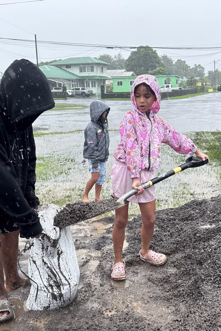 A young girl shovels wet sand into a sandbag in the rain.