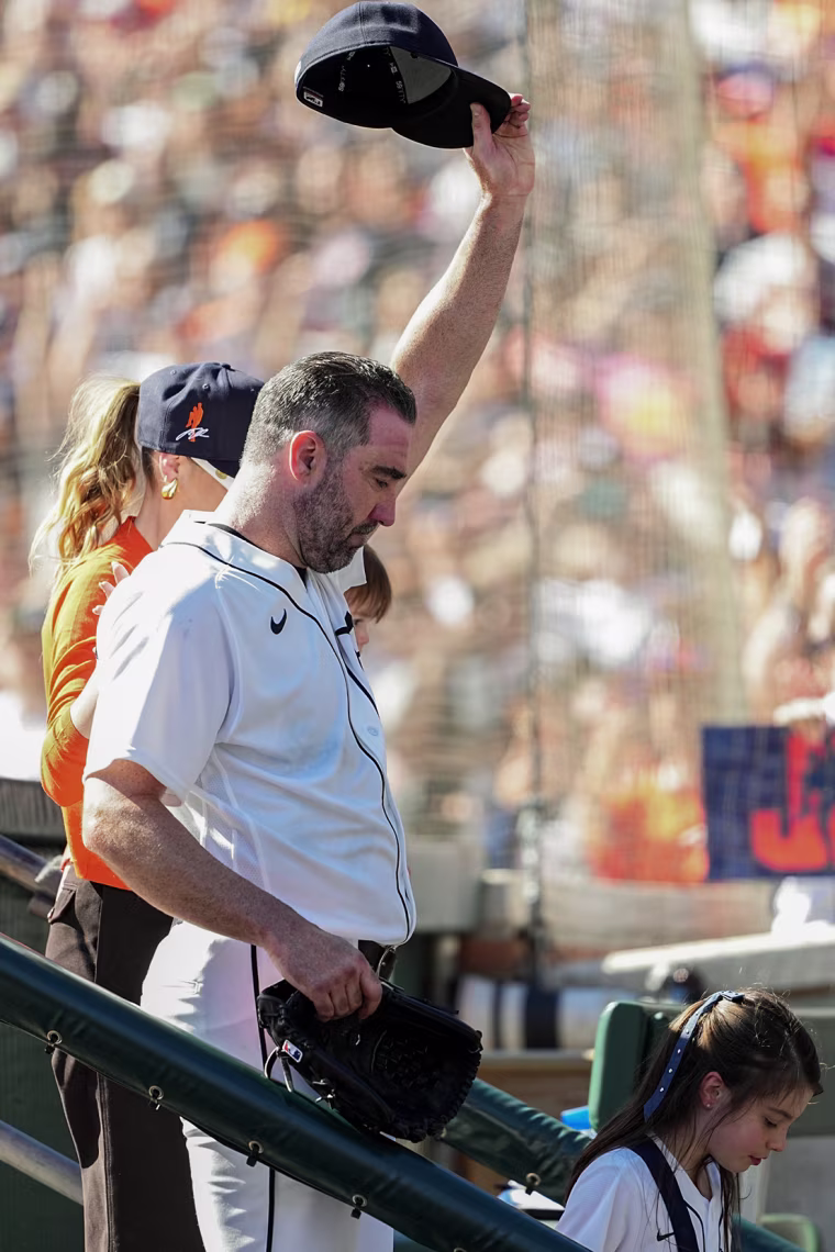 Justin Verlander steps down into a dugout with his family and holds his hat in the air.