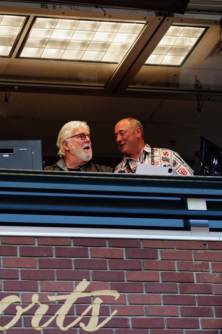 Two sports announcers speaking from their stadium booth.