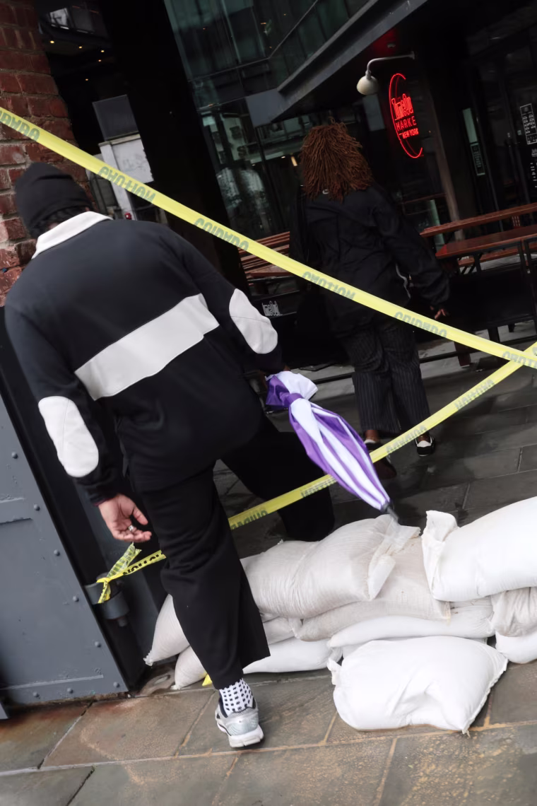 CAUTION tape in a large X shape blocking a doorway, with sandbags on the ground in front of it.