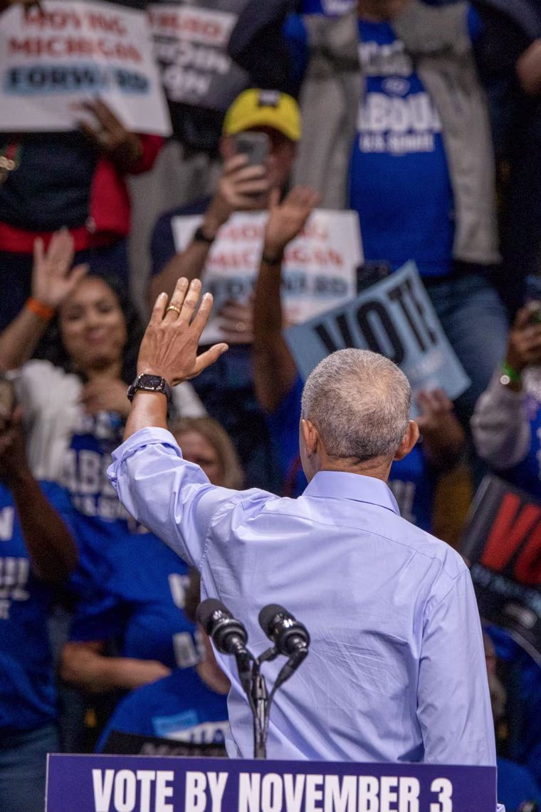 Barack Obama faces away from the camera while waving to a crowd during a rally.