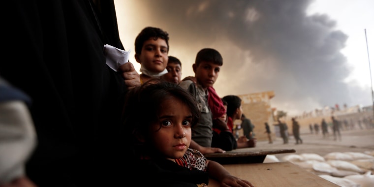 Image: Newly displaced people wait to receive food supplies at a processing center for displaced people In Qayyara