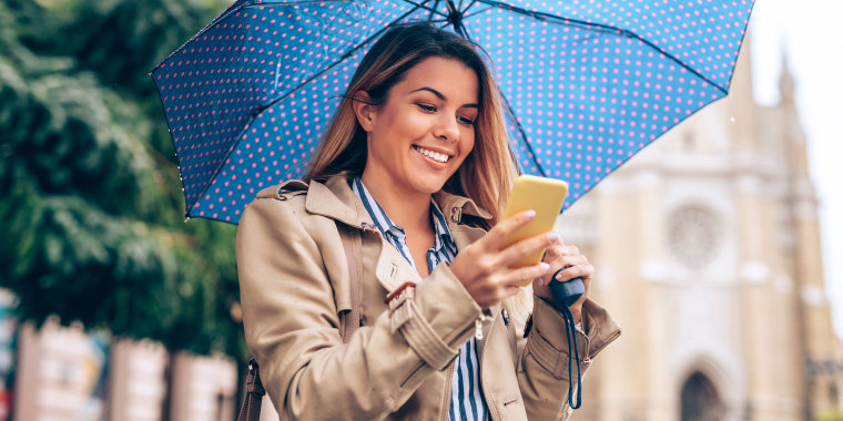 woman wearing rain jacket in rain holding umbrella and smartphone