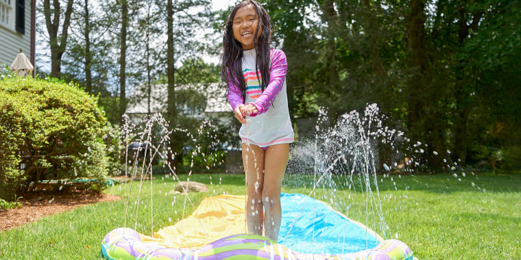 Little girl in her backyard, standing up on her blue waterslide as it squirts out water