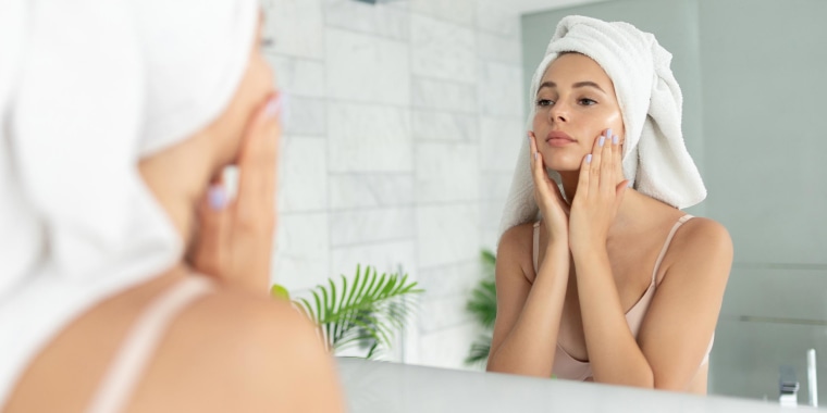 Woman using skin face cream lotion, while looking in the mirror in her bathroom