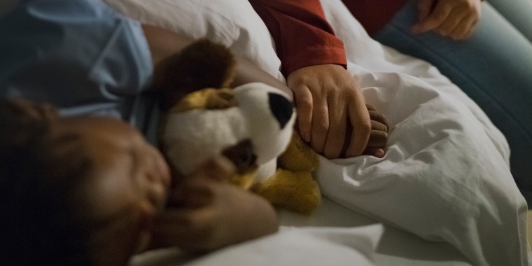 Mother holding ill son's hand sleeping on bed