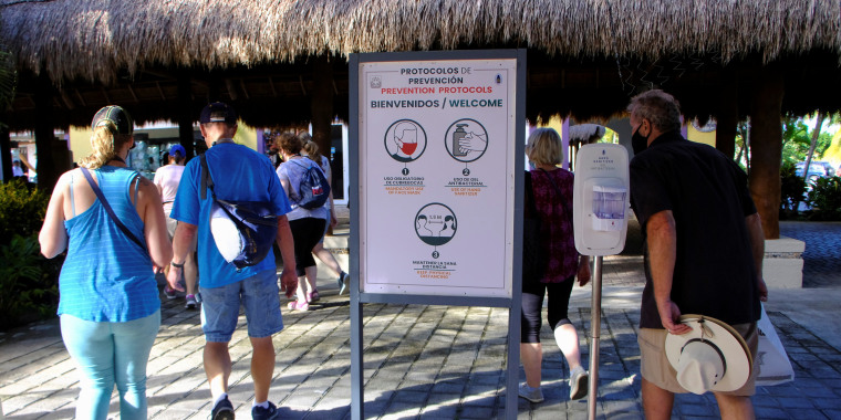 People walk past a sign with safety recommendations on Covid-19 near a dock for cruise ships, in Cozumel, Mexico, on December 6, 2021.