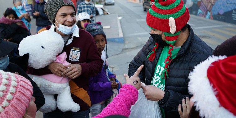 Una persona disfrazada de duende regala juguetes a migrantes, en la ciudad de Tijuana, estado de Baja California (México). En el campamento la Garita del Chaparral y el albergue Movimiento Juventud 2000, migrantes centroamericanos esperan la llegada de la Navidad, con el deseo de poder cruzar la frontera de manera legal.