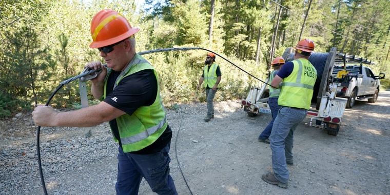 Carl Roath, left, a worker with the Mason County (Wash.) Public Utility District, pulls fiber optic cable off of a spool, as he works with a team to install broadband internet service to homes in a rural area surrounding Lake Christine near Belfair, Wash., Aug. 4, 2021.
