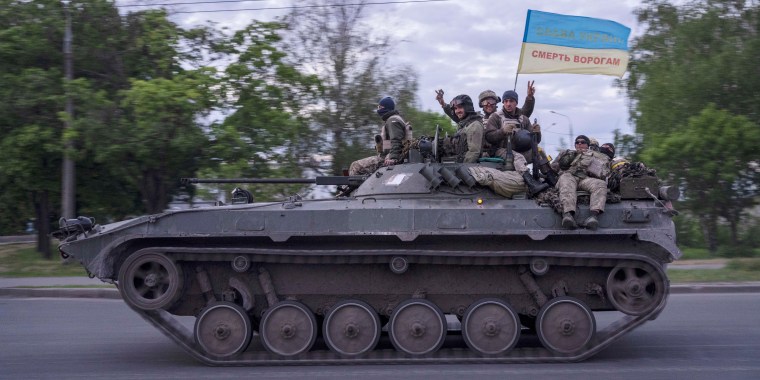 Ukrainian serviceman wave a flag which reads "Glory to Ukraine" in the Kharkiv region on May 16, 2022.