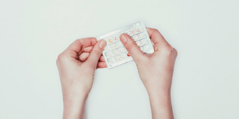 cropped shot of woman holding contraceptive pills in hands isolated on grey