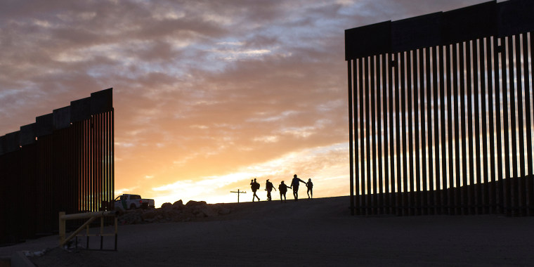 A pair of migrant families from Brazil pass through a gap in the border wall to reach the United States after crossing from Mexico to seek asylum, in Yuma, Ariz., on June 10, 2021.