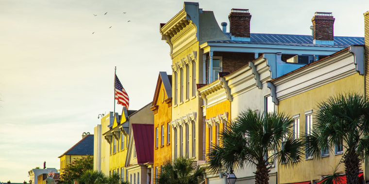 An American flag flies over the historic buildings of King Street, Charleston, bathed in evening light and fronted with palmetto trees.