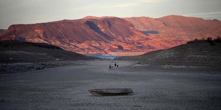People walk towards a formerly sunken boat on cracked earth hundreds of feet from what is now the shoreline on Lake Mead at the Lake Mead National Recreation Area, near Boulder City, Nev., on May 9, 2022.