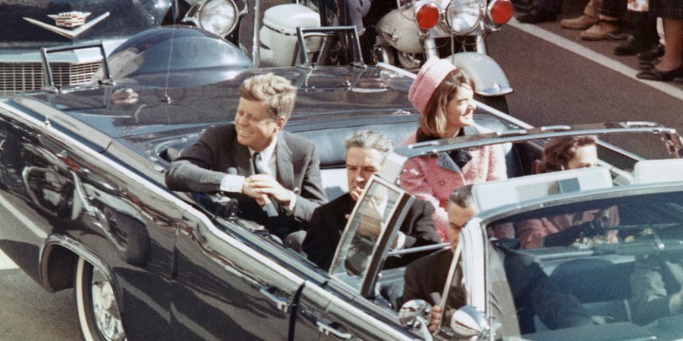 President and Mrs. John F. Kennedy smile at the crowds lining their motorcade route in Dallas, Texas