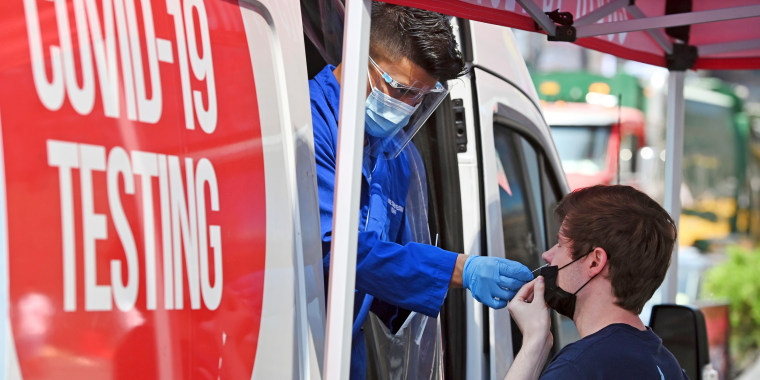 A medical technician administers a COVID-19 test to a man out of a testing truck