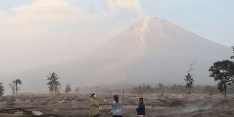 Villagers stand on an area covered in volcanic ash as Mount Semeru looms in the background in Kajar Kuning village in Lumajang, East Java, Indonesia, Monday, Dec. 5, 2022. Indonesia's highest volcano on its most densely populated island released searing gas clouds and rivers of lava Sunday in its latest eruption. (AP Photo/Imanuel Yoga)