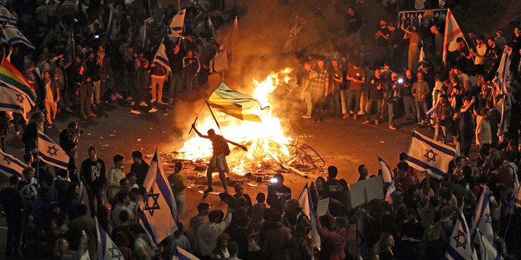 Protesters block a road and hold national flags as they gather around a bonfire during a rally against the Israeli government's judicial reform in Tel Aviv on March 27, 2023. 