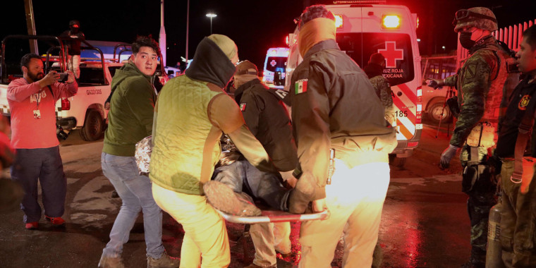 Police officers carry an injured migrant following a fire that killed dozens of migrants in Ciudad Juarez