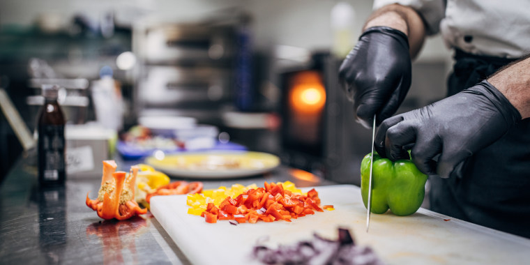 Chef in black latex gloves cutting vegetables in his kitchen in restaurant.