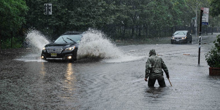 A man clears debris from a drain as a car make its way through floodwaters in Brooklyn, N.Y., on Sept. 29, 2023. 