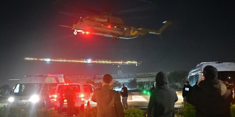 People wait at a helipad as a helicopter carrying released hostages lands