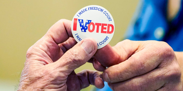 A poll worker hands a circular "I Voted" sticker to a voter