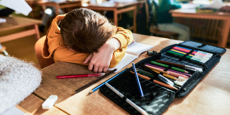 A schoolboy with head down on desk with pens scattered during class at elementary school