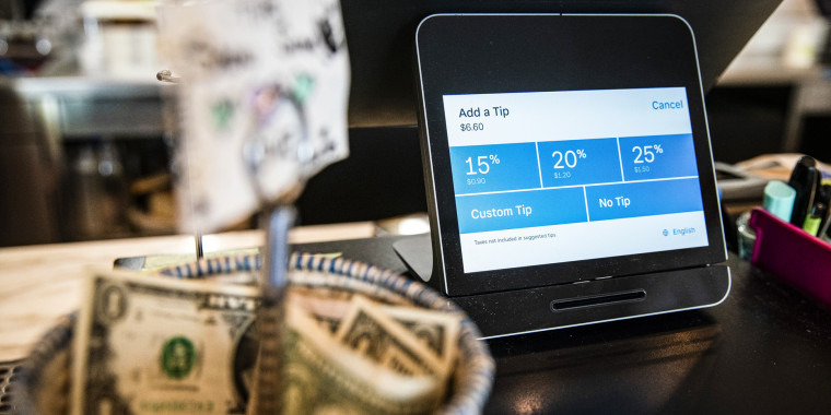 A Square payment device displays tipping options at a coffee shop next to a basket of dollar tips