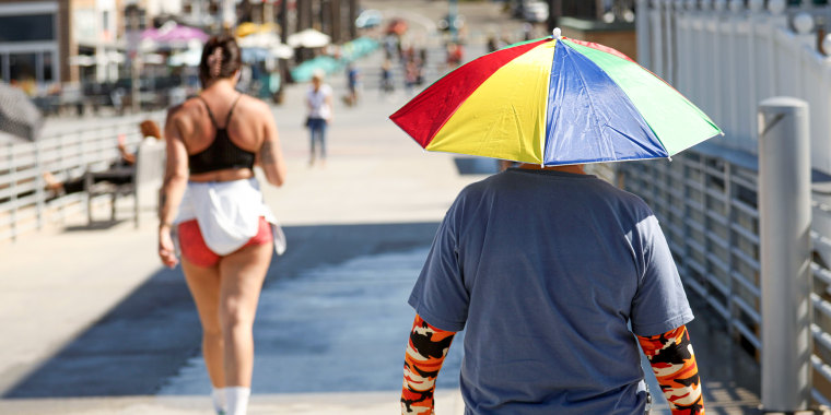A person with an umbrella hat walks in the sun.