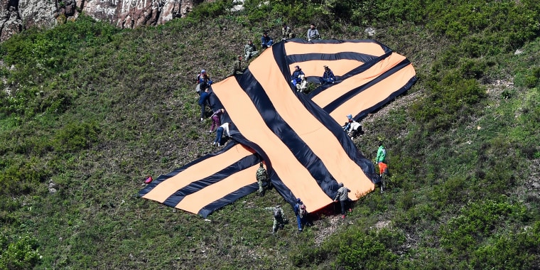 People hold a big ribbon of Saint George on a mountain slope in Divnogorsk, Russia.