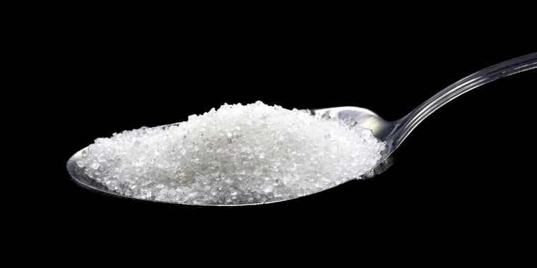 A small teaspoon with sugar, on a black background.