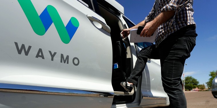 A passenger steps into a Waymo minivan parked outside