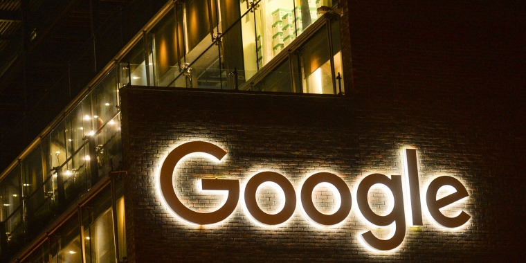 The GOOGLE logo is illuminated on a brick building at night.