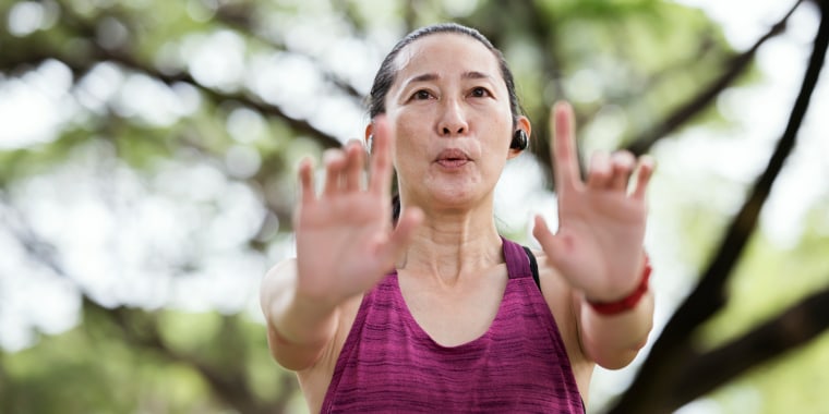Tai Chi and mind-body breathing can make you better, faster, and stronger. Middle-Aged Asian woman taking tai chi at a public park. She is practicing tai chi or qi gong poses and set her breath inhaling and exhaling.