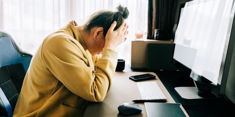 Woman working from home feeling stressed and frustrated, holding her head in her hands while sitting at her desk