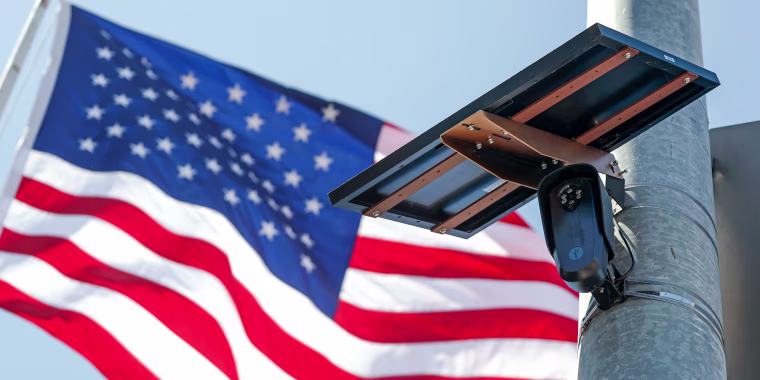An American flag flies behind a Flock Safety camera tmounted to a light pole