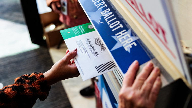 A hand places a ballot into a ballot box