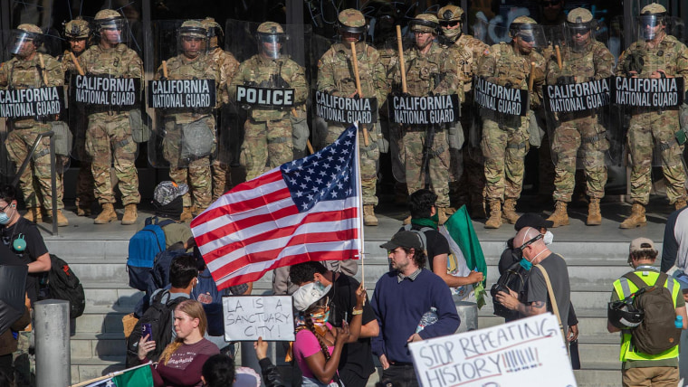 Demonstrators holding signs and flags face California National Guard members standing guard outside the Federal Building 