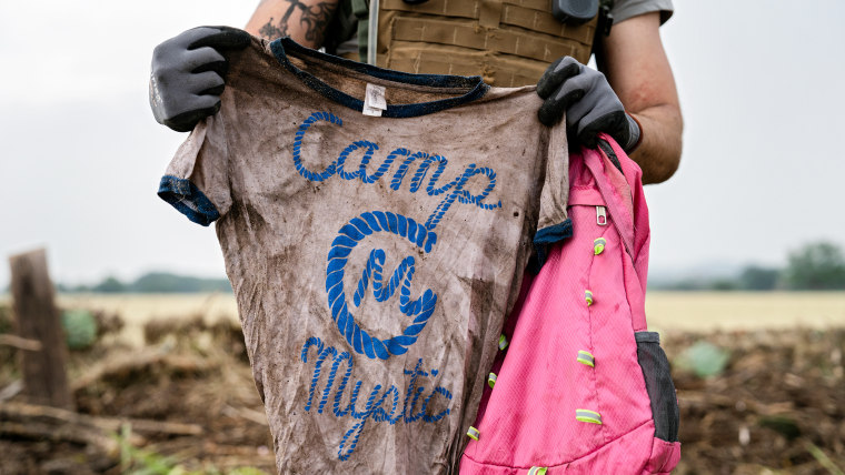 A search and rescue volunteer holds a T-shirt and backpack with the words Camp Mystic on them