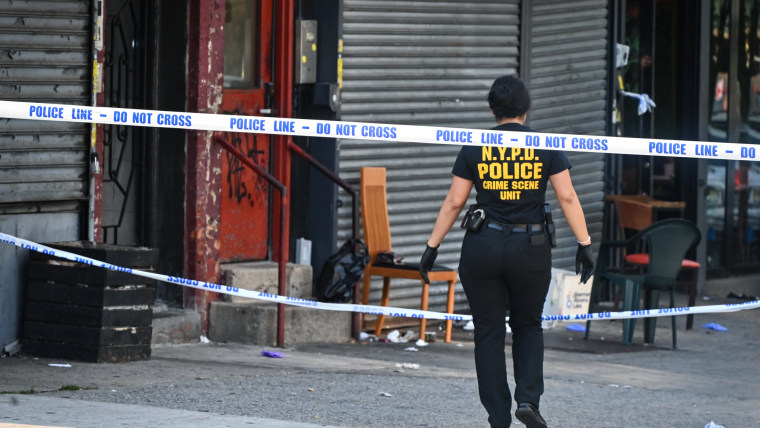 A cop walks through a crime scene on a sidewalk with police tape draped across