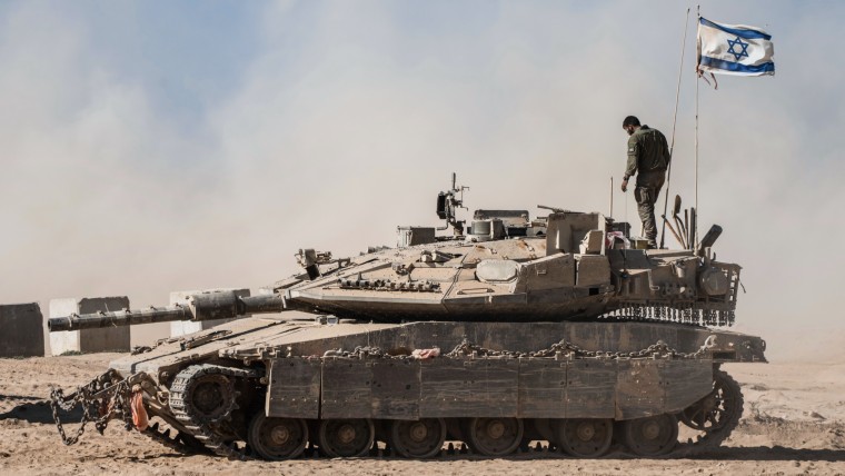 An Israeli soldier stands on the top of a tank parked