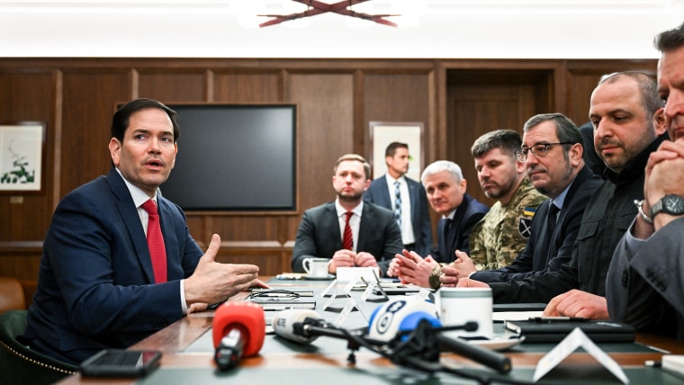 Marco Rubio, left, sits across a table with many people on the other side