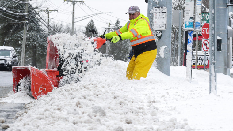 A man uses a snow blower to clear snow outside