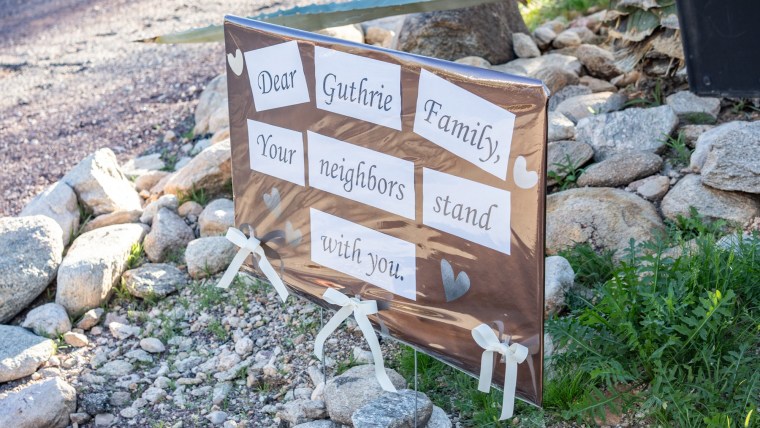 A sign posted on a front lawn that reads "Dear Guthrie family, your neighbors stand with you"