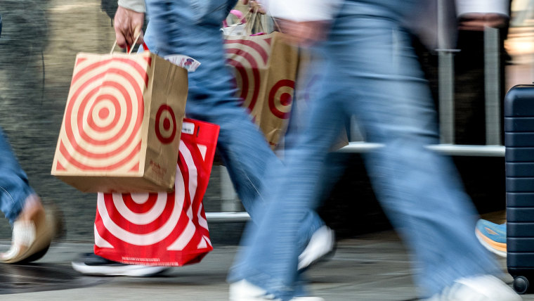 A person carrying three target bags with red spiral logos walks past in a blur on a city sidewalk.