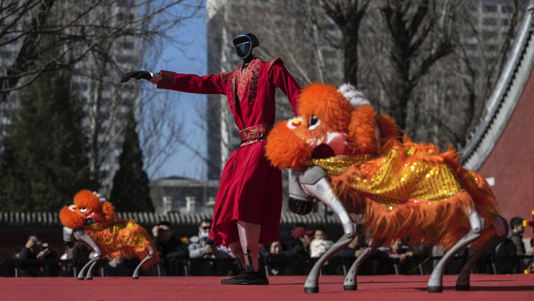 A humanoid robot and robot dogs dressed as lion dancers perform on a stage.
