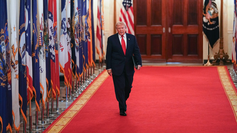 Donald Trump walks on a red carpet past a long line of U.S. state flags.